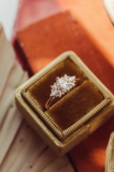 an engagement ring sits in a velvet box on top of a wooden table next to other items