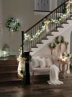 a living room filled with furniture and christmas lights on the staircase railing, along with wreaths hanging from the banister