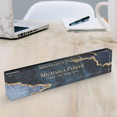 a book sitting on top of a wooden table next to a cup and laptop computer