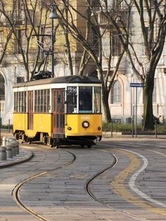 a yellow trolley car traveling down a street next to a tall white building and trees