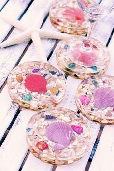 four wine glasses with seashells and shells in them on a wooden table next to a starfish