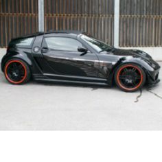 a black sports car with orange rims parked in front of a garage door,