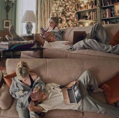 two people laying on couches in front of a christmas tree with a laptop computer