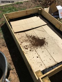 a wooden box with dirt in it sitting on the ground next to a wheelbarrow