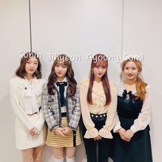 four young women standing next to each other in front of a white wall with words written on it