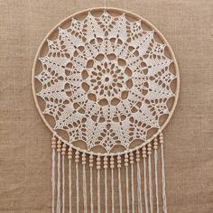 a white doily with wooden beads and tassels hanging from the side on a wall