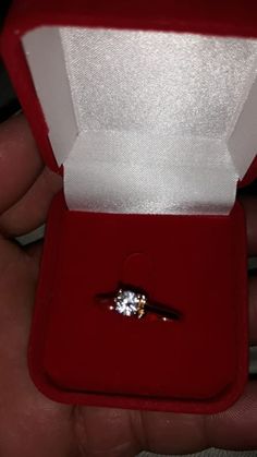 someone is holding an engagement ring in a red velvet box with a white diamond on it