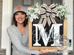 a woman holding up a framed monogrammed door hanger with flowers on it