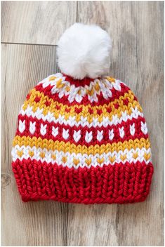 a red and yellow knitted hat with a white pom - pom