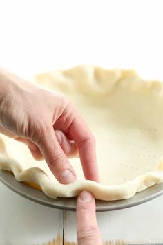 a person pressing the end of a pie crust on top of a metal pan with one hand