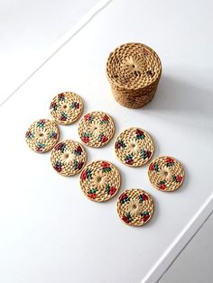 several woven buttons sitting on top of a white table next to a basket and bowl