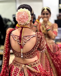 two women dressed in red and gold outfits, one wearing a flower on her head