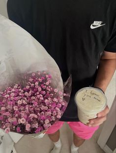 a man holding a bouquet of pink flowers and a cup of coffee in his hand