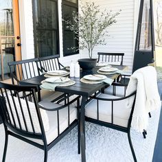 a table and chairs on a porch with white walls, black iron frame furniture and a potted plant in the center