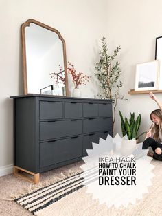 a woman is sitting on the floor in front of a dresser and mirror with plants