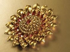 a gold brooch with red stones in the shape of a flower on a beige background