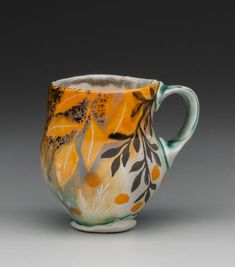 an orange and white coffee cup with leaves painted on the side, sitting in front of a gray background