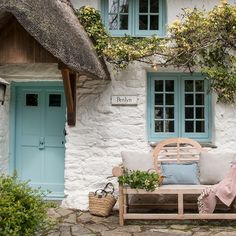 a wooden bench sitting in front of a white building with blue doors and windows on it