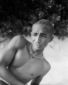 a black and white photo of a man with no shirt on sitting in the sand