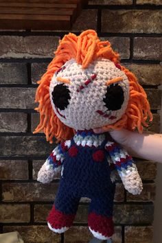 a crocheted doll with orange hair and black eyes is posed in front of a brick wall