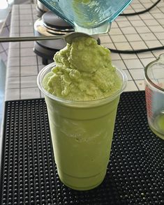 a green drink being poured into a cup with ice cream in it on a table