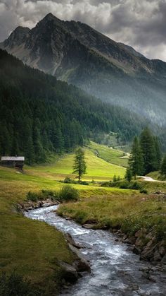 a stream running through a lush green valley under a mountain covered in mist and clouds