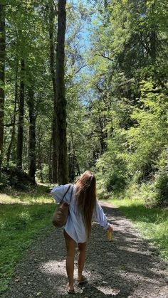 a woman walking down a dirt road in the woods with her back to the camera