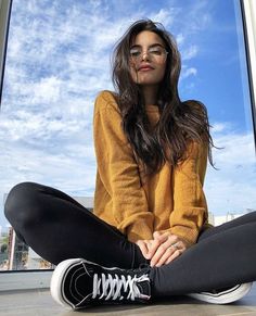 a woman sitting on the floor in front of a window with her legs crossed and wearing black leggings