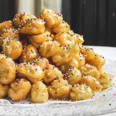 a pile of donuts with sprinkles on a white plate next to a window