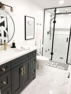 a white bathroom with black and gold accents on the vanity, shower door, and toilet