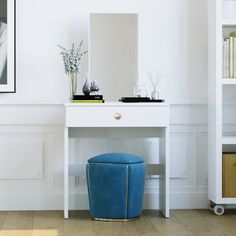 a white desk with a blue stool in front of it and a mirror on the wall