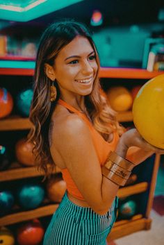 a woman holding a yellow ball in her right hand and smiling at the camera with other bowling balls behind her