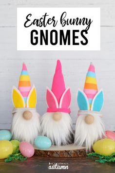 three easter bunny gnomes sitting on top of a wooden table with colorful eggs around them