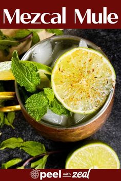 a glass filled with ice and limes on top of a table next to some mint leaves