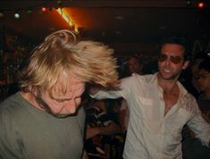 two men dancing at a party with one holding his hair in the air and smiling