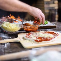 a person making pizzas on top of a wooden table next to other food items