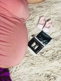 a pregnant woman laying on top of a white rug next to a pair of baby shoes