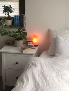 a bed with white sheets and pillows next to a night stand with a lit candle on it