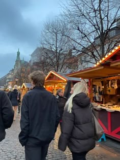 two people walking down the street in front of a christmas market