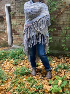 a woman is standing in the leaves wearing a shawl with fringes on it