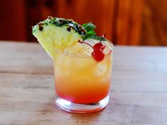 a pineapple and cherry cocktail with garnishes on the rim, sitting on a wooden table