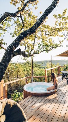 a woman sitting in a hot tub on top of a wooden deck next to a tree