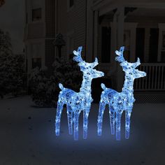 two lighted reindeer statues in front of a house with snow on the ground and trees