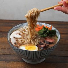 someone is holding chopsticks above a bowl of ramen with meat and vegetables