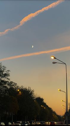 the sun is setting over a street with cars parked on it and an airplane flying in the sky