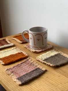 a coffee cup sitting on top of a wooden table next to four knit coasters