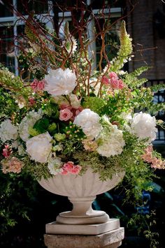 a vase filled with lots of flowers sitting on top of a white pedestal next to a tree