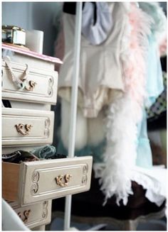 a white dresser with lots of drawers and clothes hanging on the wall next to it