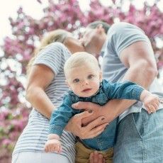 a man and woman holding a baby in front of a tree with pink flowers on it