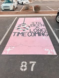 an empty parking lot with a pink painted sign that says it's been a long time coming